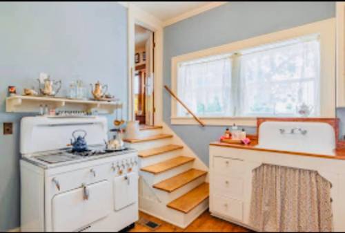 A cozy kitchen with a vintage stove, a farmhouse sink, and wooden stairs leading to an upper level.