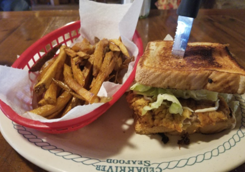A plate with a toasted sandwich filled with lettuce and fried chicken, accompanied by a basket of golden fries.