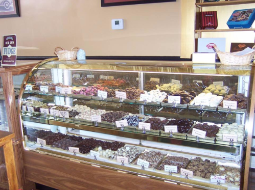 A display case filled with various types of fudge and chocolates, neatly arranged with labels.