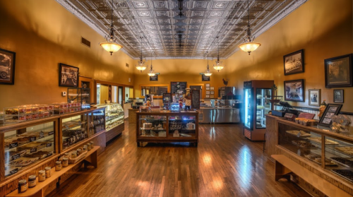A cozy café interior with wooden floors, display cases of treats, and vintage decor under ornate ceiling lights.