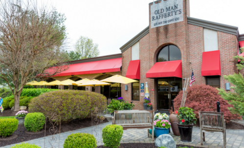 Exterior of Old Man Rafferty's restaurant featuring red awnings, outdoor seating, and landscaped greenery.