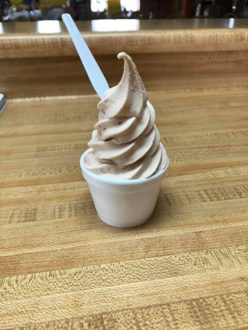 A soft-serve ice cream cone in a small cup, swirled with a light brown color, sitting on a wooden countertop.