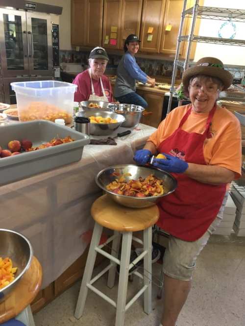 A group of people preparing food in a kitchen, with one woman smiling while cutting fruit in a bowl.