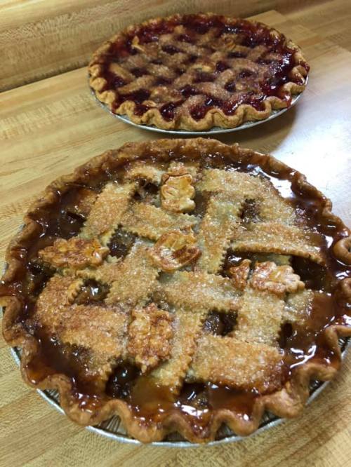 Two homemade pies on a wooden surface: one with a lattice crust and cherry filling, the other with a shiny apple filling.