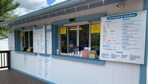 A colorful ice cream stand with menus for ice cream, sundaes, and toppings displayed on the walls.