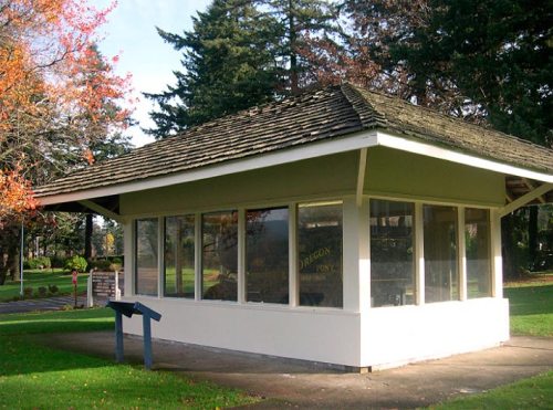 A small, modern building with large windows, surrounded by trees and grass in a park setting.