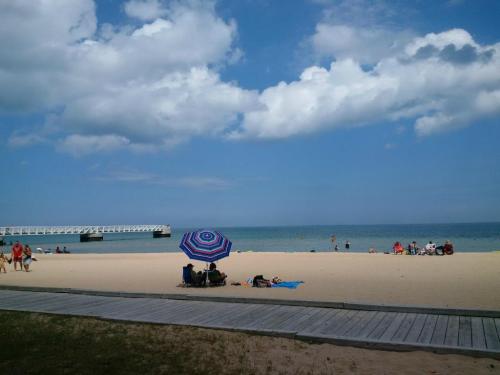 A sunny beach scene with people relaxing under umbrellas, a pier in the background, and fluffy clouds in the sky.