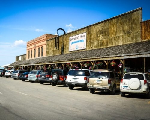 A rustic storefront with a wooden facade and parked vehicles lined up in front under a clear blue sky.