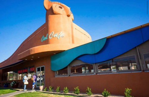 A colorful café building shaped like a cow, with a blue wave design and two people standing outside.