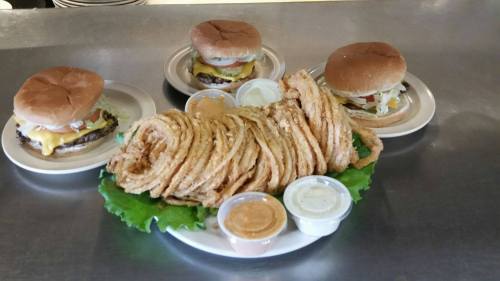 Three burgers with toppings and a large serving of onion rings on a platter, accompanied by dipping sauces.