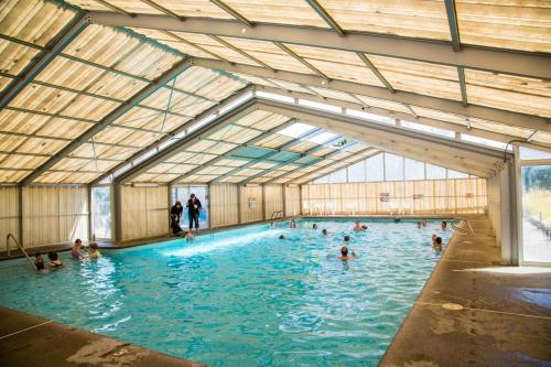 Indoor swimming pool with people swimming and relaxing, surrounded by large windows and a bright, airy atmosphere.