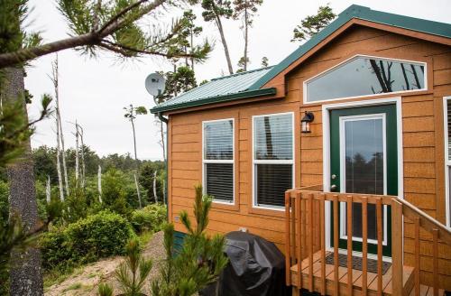 A cozy wooden cabin with a green roof, porch, and satellite dish, surrounded by trees and greenery.