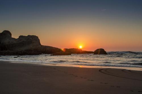 Sunset over a tranquil beach, with gentle waves lapping at the shore and rocky formations silhouetted against the sky.