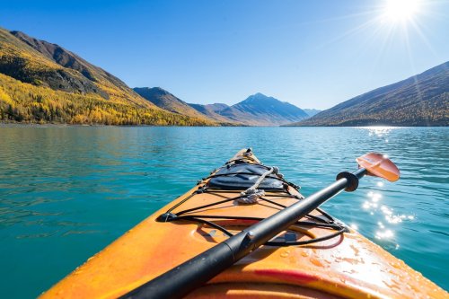A kayak on calm turquoise water, surrounded by mountains and autumn foliage under a clear blue sky.