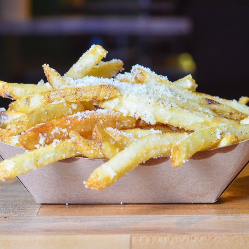 A serving of golden, crispy French fries topped with grated cheese in a brown paper tray.