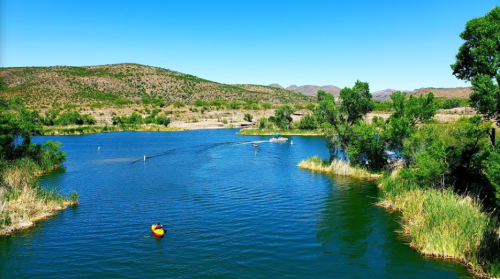 A serene river scene with a kayaker, lush greenery, and distant hills under a clear blue sky.