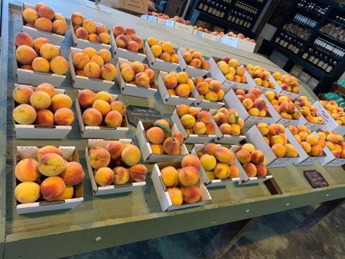 A display of fresh peaches in white boxes on a wooden table at a market.