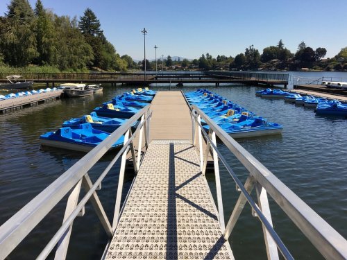 A dock with blue paddle boats lined up on calm water, surrounded by trees and a clear blue sky.
