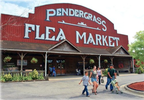 A group of people walking towards the Pendergrass Flea Market, featuring a large red building with white lettering.