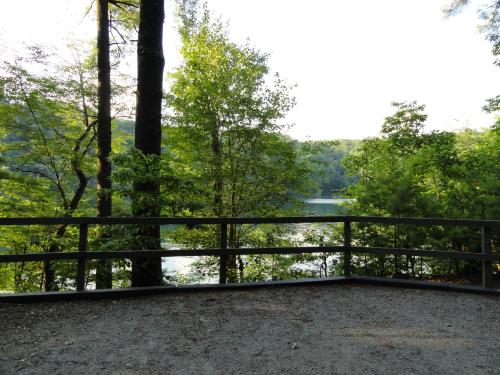 A serene view of a lake surrounded by lush green trees, framed by a wooden railing in a peaceful outdoor setting.