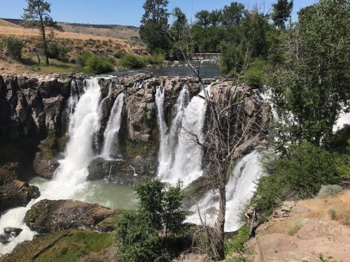 A scenic view of a waterfall cascading over rocky cliffs, surrounded by lush greenery and trees.