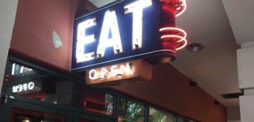 Neon sign reading "EAT" with "OPEN" below, illuminating a restaurant entrance.