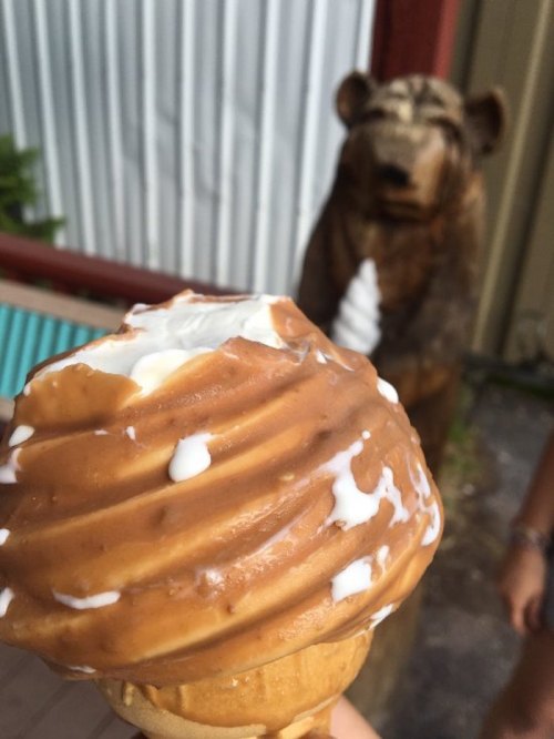 A close-up of a swirled ice cream cone with a bear statue in the background.