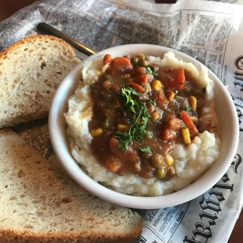 A bowl of mashed potatoes topped with vegetable gravy, served with slices of bread on the side.