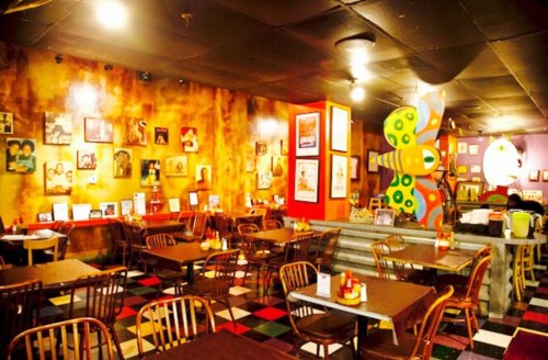 Colorful restaurant interior with wooden tables, chairs, and a vibrant wall adorned with framed photos and artwork.