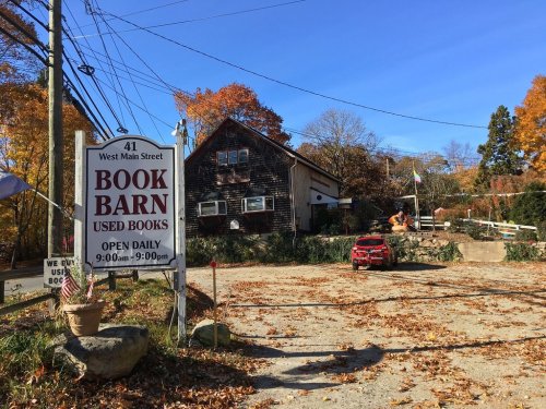 A rustic book barn with a sign reading "Used Books" surrounded by autumn foliage and a clear blue sky.
