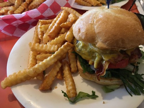 A juicy cheeseburger with lettuce, tomato, and bacon, served with a side of crispy crinkle-cut fries on a plate.
