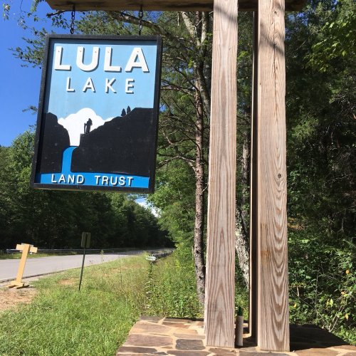 Sign for Lula Lake Land Trust, featuring a silhouette of a person near a waterfall, surrounded by trees and blue sky.