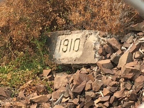 A weathered stone marker displaying the year "1910" surrounded by rocks and dry vegetation.