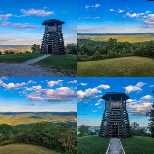 A scenic view of a wooden observation tower surrounded by lush greenery and rolling hills under a blue sky.