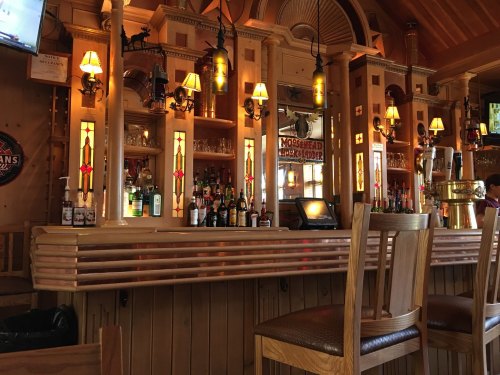 A cozy wooden bar with warm lighting, shelves of liquor, and decorative lamps in a rustic setting.