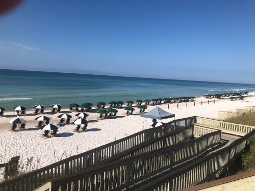 A serene beach scene with green umbrellas and chairs on white sand, calm blue water, and a clear sky.