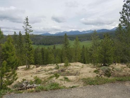 A scenic view of a green valley surrounded by trees and mountains under a cloudy sky.