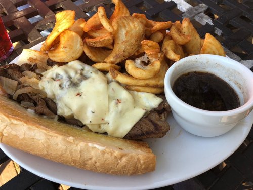 A plate with a cheesy beef sandwich, curly fries, and a small bowl of dipping sauce.