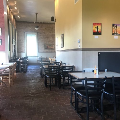 Interior of a restaurant with empty tables, brick walls, and artwork on display. Bright and inviting atmosphere.