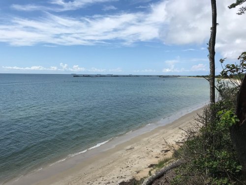 A serene beach scene with calm waters, sandy shore, and a clear blue sky dotted with clouds.