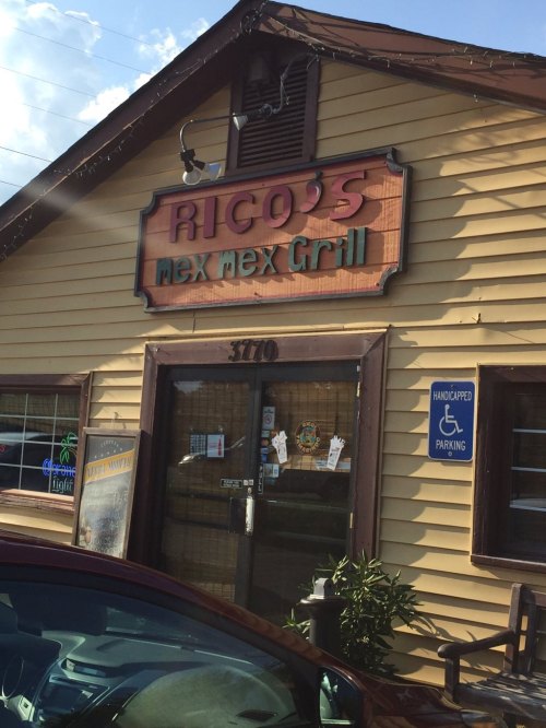 Sign for Rico's Mex Mex Grill on a wooden building, featuring a handicapped parking sign nearby.