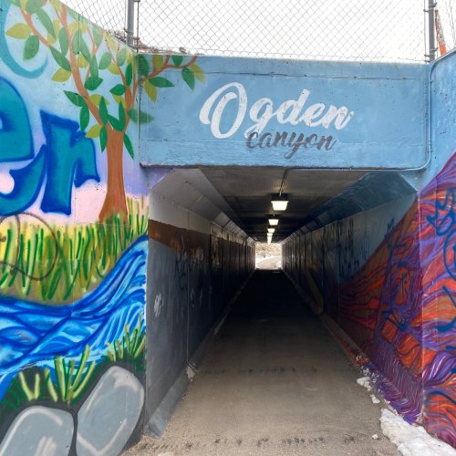 A colorful mural in a tunnel, featuring "Ogden Canyon" text, with trees and a river painted on the walls.
