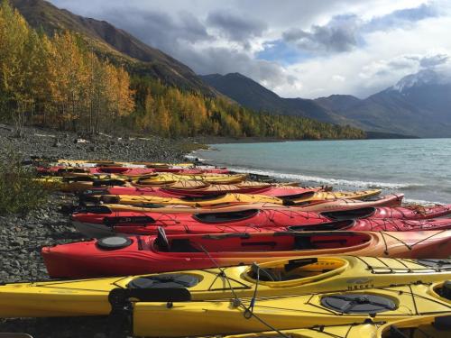 Colorful kayaks in red and yellow lined up on a rocky shore, with autumn trees and mountains in the background.