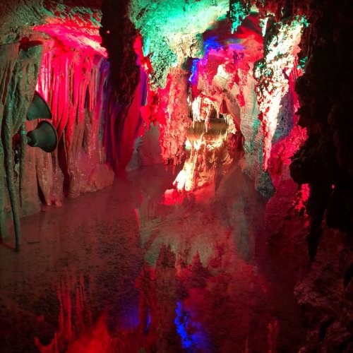 Colorful cave interior with red and green lights reflecting off water, creating a mystical atmosphere.