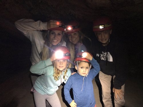 A group of five people, including children, wearing helmets with lights, smiling in a cave setting.