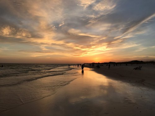 A serene beach at sunset, with silhouettes of people walking along the shore and colorful clouds in the sky.
