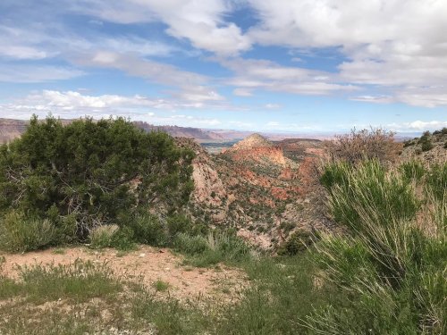 A scenic view of rugged mountains and valleys under a partly cloudy sky, with greenery in the foreground.