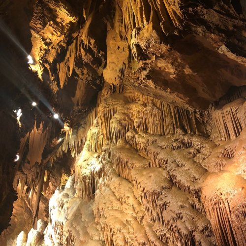 Stalactites and stalagmites in a cave, illuminated by soft lights, showcasing intricate rock formations.