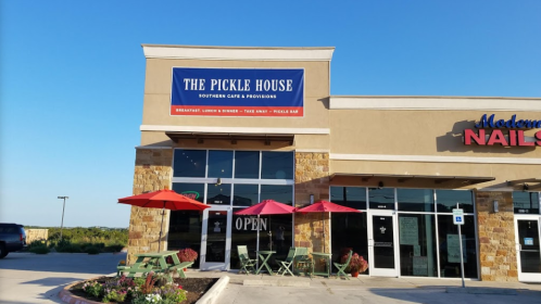 Exterior of The Pickle House, a southern café with outdoor seating and a bright blue sky in the background.