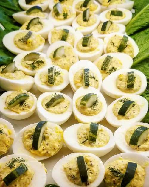 A platter of deviled eggs topped with dill and cucumber slices, arranged on a bed of lettuce.